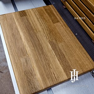 May include: A rectangular wooden board made of joined light brown oak planks with a visible natural grain pattern. The board features the text 24-005 in the upper right corner and the logo HJ HILT Woodworking in the bottom right corner.