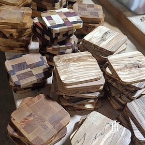 Könnte beinhalten: Eine Sammlung handgefertigter Holzuntersetzer in verschiedenen Designs. Einige Untersetzer weisen ein Patchworkmuster aus verschiedenen Holzarten auf, während andere die natürliche Holzmaserung zeigen. Die Untersetzer sind quadratisch oder leicht abgerundet und haben eine rustikale Ästhetik.