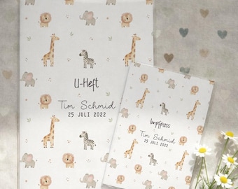 May include: Two white baby record books with a safari animal pattern. The books feature giraffes, lions, elephants, and zebras. The larger book says "U-Heft" and the smaller book says "Impfpass". Both books have the name "Tim Schmid" and the date "25 JULI 2022".