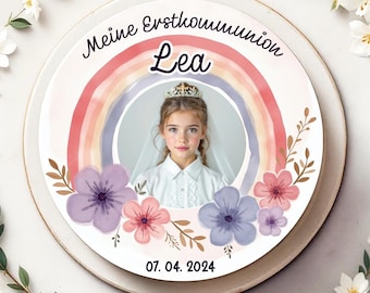 Puede incluir: Un pastel redondo blanco decorado con un arcoíris, flores y el texto "Meine Erstkommunion Lea 07.04.2024". Una foto de una niña con un vestido blanco y una corona está en el centro del pastel.