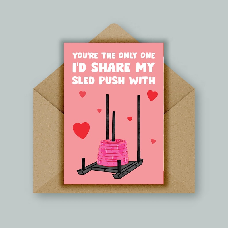 Pu&ograve; includere: Un biglietto rosa di San Valentino con il testo "Sei l'unico con cui condividerei la mia spinta di slitta." La carta presenta un'illustrazione di cartone animato di una slitta con pesi rosa.