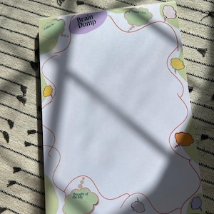 May include: A white notepad with the words "Brain Dump" in purple and "Today I feel..." and "Thought of the day" in green. The notepad has a red line design with colourful thought bubbles.