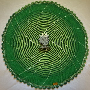 May include: Green crocheted doily with a spiral pattern and a green and white gradient. A silver Rick and Morty character is in the center of the doily.