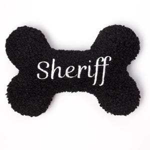 Könnte beinhalten: Schwarzes Plüsch-Hundespielzeug in Knochenform mit dem in Weiß gestickten Wort "Sheriff".