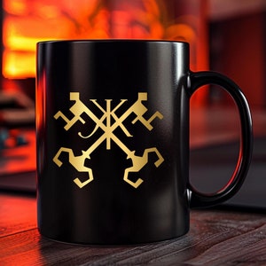 Op de afbeelding: Zwarte keramische mok met een gouden ontwerp van vier gekruiste sleutels in het midden. De sleutels zijn gestileerd en hebben een decoratieve versiering aan de bovenkant. De mok heeft een handvat aan de rechterkant.