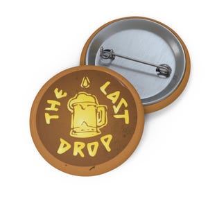 May include: A brown button with a yellow beer mug graphic and the text "The Last Drop".