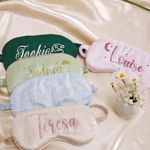 May include: Five personalised sleep masks in various colours, including green, light green, blue, beige, and pink. Each mask has a different name embroidered on it, including "Tookie", "Sydney", "Mrs. Burge", "Teresa", and "Louise".
