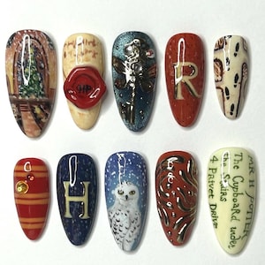 Puede incluir: Un conjunto de diez uñas pintadas en forma de almendra. Cada uña presenta un diseño diferente, incluyendo un sello de cera rojo con "HP", un búho nival y la letra "H". Las uñas están decoradas con varios colores y texturas.
