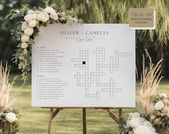 May include: A white crossword puzzle with black text on a white easel. The puzzle is titled "Oliver + Camelia Sip & Solve". The crossword puzzle is a wedding game for guests to play.