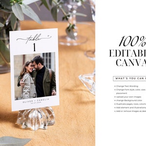 May include: A white card with a black script font that says "table 1" and a photo of a couple. The card is on a clear glass stand. The text "Oliver + Camelia 03.21.2023" is at the bottom of the card.