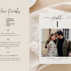 May include: A white table number card with a black handwritten font that says "table 1". A small heart symbol is next to the number. A photo of a couple is below the table number. The photo shows a man and woman embracing. The text below the photo says "OLIVER + CAMELIA 03.27.2029".