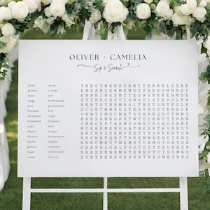 May include: A white sign with black text, featuring a wedding word search puzzle. The puzzle includes words like "bride", "groom", "love", "ceremony", "reception", "cake", "dance", "flowers", "music", "guests", "toast", "venue", "dress", "tuxedo", "veil", "bridesmaid", "groomsman", "kiss", "rings", "bouquet", "aisle", "chapel", "honeymoon", "couple", "romance", "celebration", "forever". The sign also includes the names "Oliver" and "Camelia" and the phrase "Sup & Search".