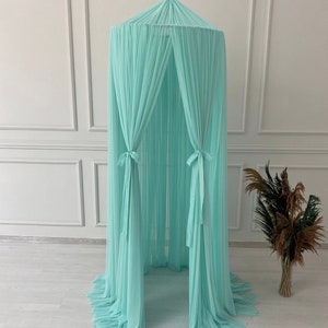 May include: A light turquoise canopy bed net with a round top and flowing fabric. The net hangs from a single point, with the fabric gathered and tied at intervals. The canopy is designed for a bed or play area.