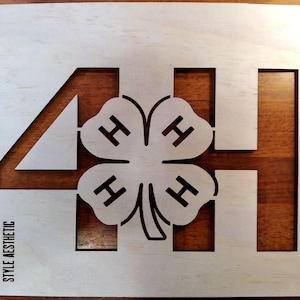 May include: A wooden stencil featuring the number 4, the letters H, and a four-leaf clover design. The text "MERRILL'S STYLE AESTHETIC" is printed in the lower left corner. The stencil is light-colored with a dark brown background.