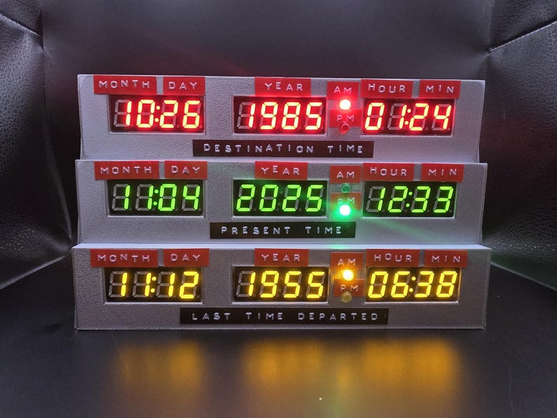 May include: A three-tiered digital time display unit featuring red, green, and yellow LED readouts. Each tier is labeled with Month, Day, Year, Hour, and Min, with text plates reading Destination Time, Present Time, and Last Time Departed.
