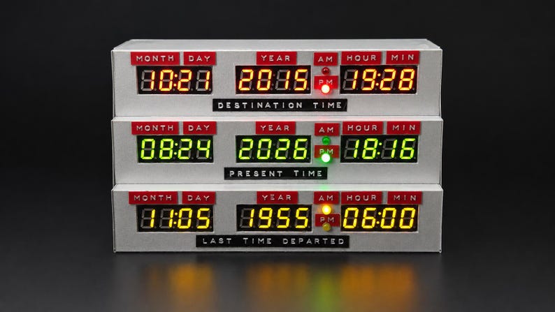 May include: A three-tiered digital time display unit with a silver finish. Each row features red labels for Month, Day, Year, AM, PM, Hour, and Min. The top row shows Destination Time, the middle Present Time, and the bottom Last Time Departed.