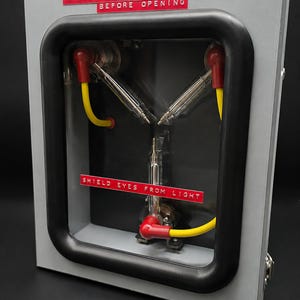Three-quarter view of the Flux Capacitor showing the metal case, clear window and warning labels
