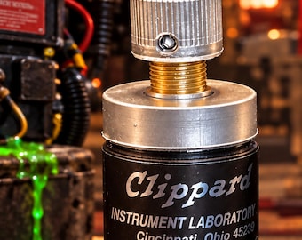 Puede incluir: Un componente cilíndrico negro Clippard Instrument Laboratory Minimatic con una perilla superior plateada estriada y un cuello roscado dorado. El cuerpo presenta texto blanco que dice Clippard Instrument Laboratory Cincinnati, Ohio 45239 Minimatic U.S. PAT. NO'S 3.766.935: 3.766.831.