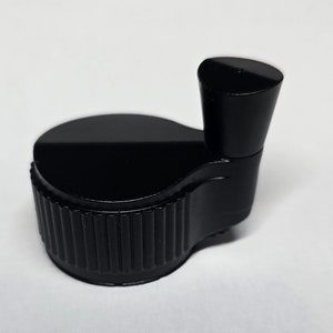 Op de afbeelding: Zwarte plastic knop met een geribbelde basis en een gladde, afgeronde bovenkant.