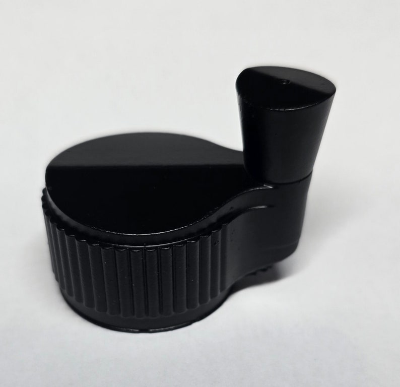 Op de afbeelding: Zwarte plastic knop met een geribbelde basis en een gladde, afgeronde bovenkant.