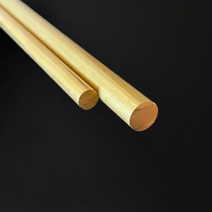 Può includere: Due barre di ottone di diametro diverso, una è leggermente più grande dell'altra. Entrambe le barre sono lucide e hanno un colore dorato.