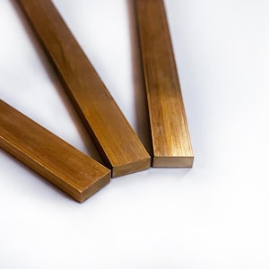 May include: Three rectangular pieces of brass, each with a different length, are arranged in a triangular shape on a white surface.