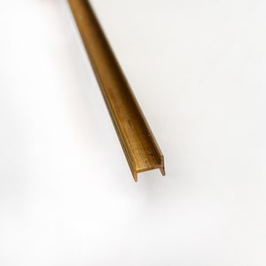 Puede incluir: Un perfil en U de metal dorado, un tipo de moldura utilizado en la construcción y el diseño.
