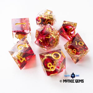 Puede incluir: Juego de siete dados poliédricos con esquema de color rojo y dorado. Los dados transparentes tienen inclusiones rojas y números dorados. Diseñados para juegos de rol de mesa.