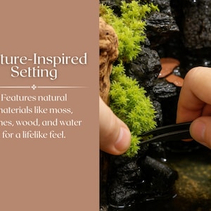 May include: A close-up of a hand using tweezers to arrange moss on a rock. The moss is green and the rock is black. The background is a brown surface with the text "Nature-Inspired Setting" and "Features natural materials like moss, stones, wood, and water for a lifelike feel."