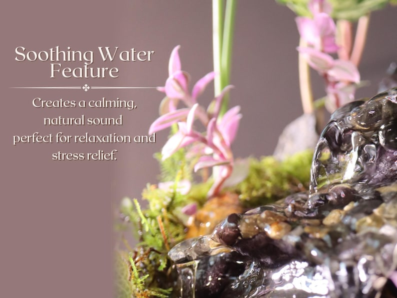 May include: A small tabletop water fountain with a cascading waterfall effect. The fountain is surrounded by green moss and pink flowers. The text "Soothing Water Feature" is displayed above the fountain. The text "Creates a calming, natural sound perfect for relaxation and stress relief." is displayed below the fountain.