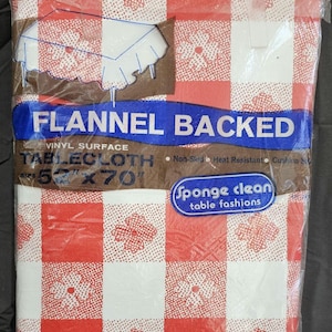 May include: A red and white checkered flannel-backed vinyl tablecloth in its original packaging. The tablecloth is 52" x 70" and features a floral pattern within the checkered squares. The packaging includes the text "FLANNEL BACKED" and "TABLECLOTH".