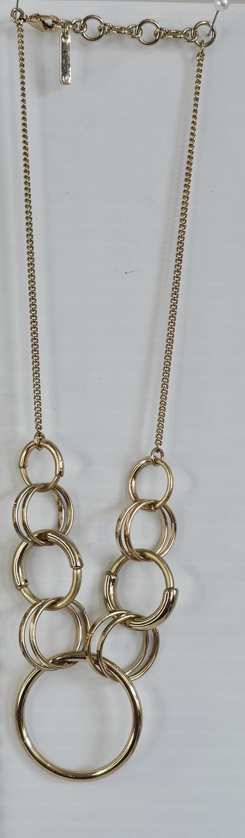 May include: Gold-toned necklace featuring a chain and multiple linked circles. The necklace has a delicate chain and a series of interconnected, large circular links. The jewelry is displayed against a white background.