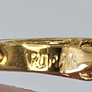 May include: Close-up of a gold-colored jewelry clasp with the engraved text "ROMA". The clasp has a detailed design and a shiny finish, suggesting a vintage or high-end piece. The background is a neutral color.