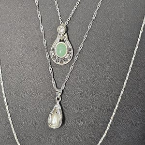 Peut inclure: Un collier argent&eacute; &agrave; trois rangs avec trois pendentifs. Le pendentif sup&eacute;rieur pr&eacute;sente une pierre verte entour&eacute;e de pierres plus petites. Le pendentif du milieu est en forme de larme avec une perle &agrave; l'int&eacute;rieur. Le pendentif inf&eacute;rieur est une simple cha&icirc;ne en argent.