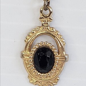 May include: A gold-toned pendant necklace featuring an oval black gemstone. The pendant has an ornate, vintage design with a decorative frame and a delicate chain.