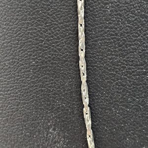 Peut inclure: Un collier en cha&icirc;ne argent&eacute;e de style cha&icirc;ne &agrave; maillons. La cha&icirc;ne est sur un fond noir.