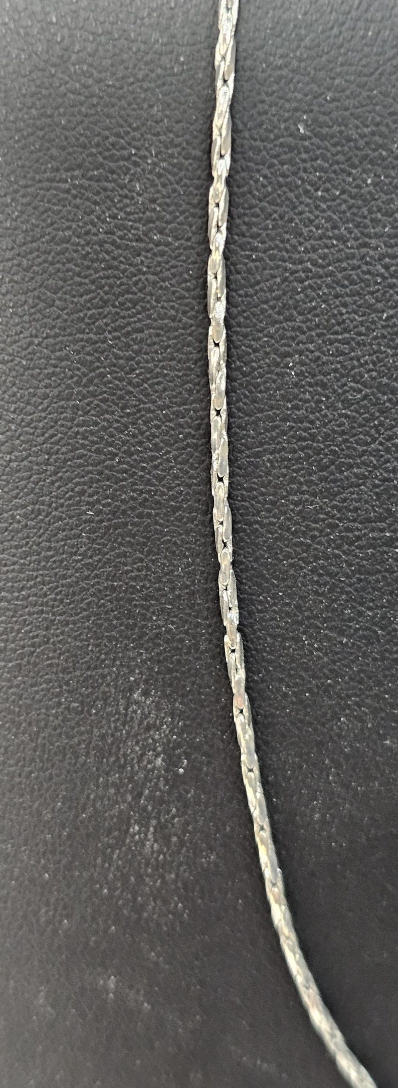 Peut inclure: Un collier en cha&icirc;ne argent&eacute;e de style cha&icirc;ne &agrave; maillons. La cha&icirc;ne est sur un fond noir.