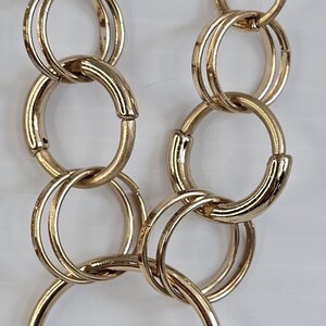 May include: Gold-toned necklace featuring a chain and multiple interlocking circular links. The necklace has a polished finish and hangs against a white background. The design is simple yet elegant, suitable for various occasions.