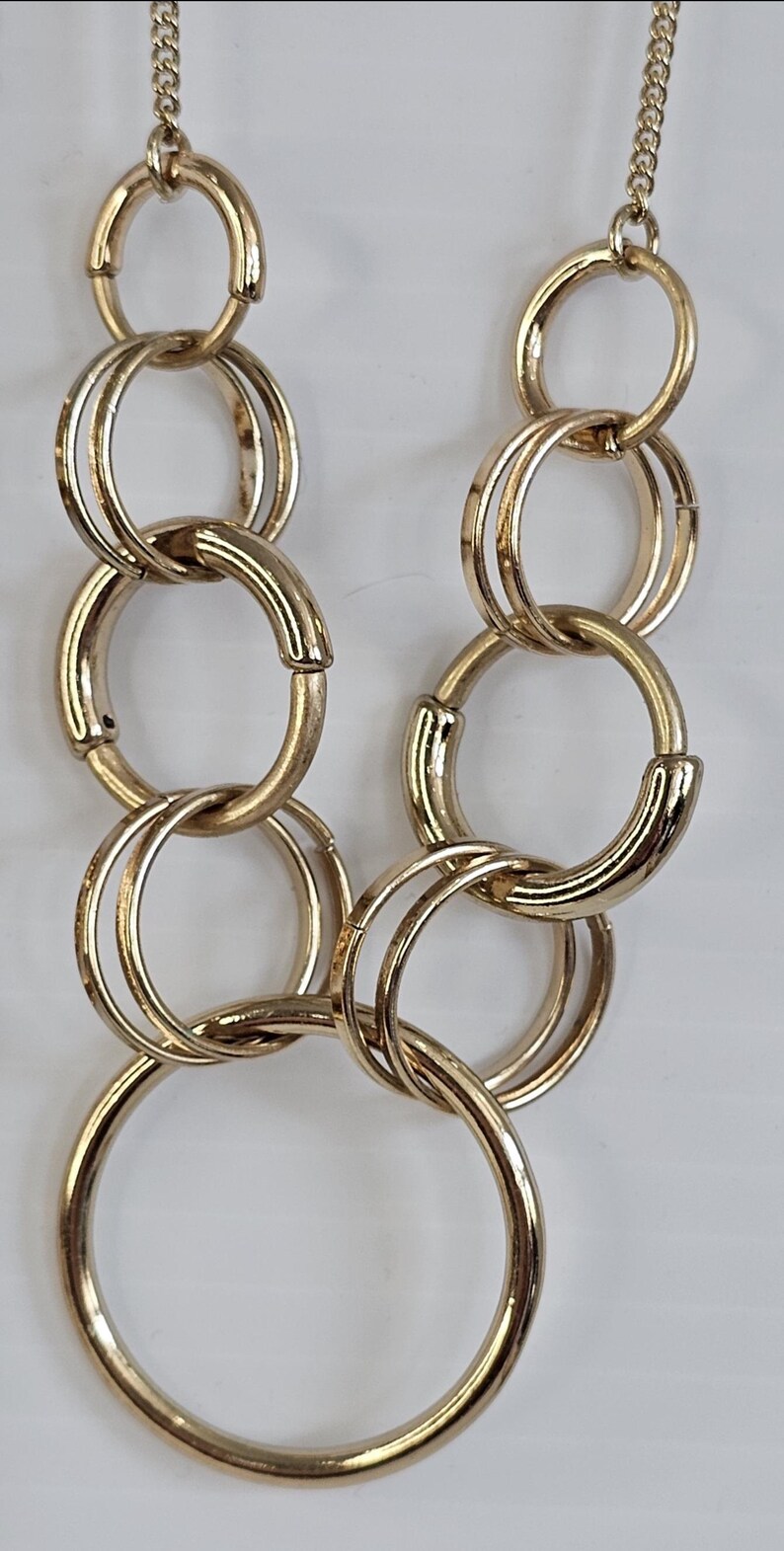 May include: Gold-toned necklace featuring a chain and multiple interlocking circular links. The necklace has a polished finish and hangs against a white background. The design is simple yet elegant, suitable for various occasions.