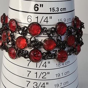 May include: A vintage bracelet with dark metal links and vibrant red, faceted, round gemstones. The bracelet is shown on a measuring tool, with measurements in inches and centimeters.