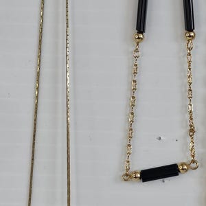 May include: A collection of gold-toned necklaces. One features a teardrop-shaped pendant, while others have delicate chains. One necklace has black rectangular beads.