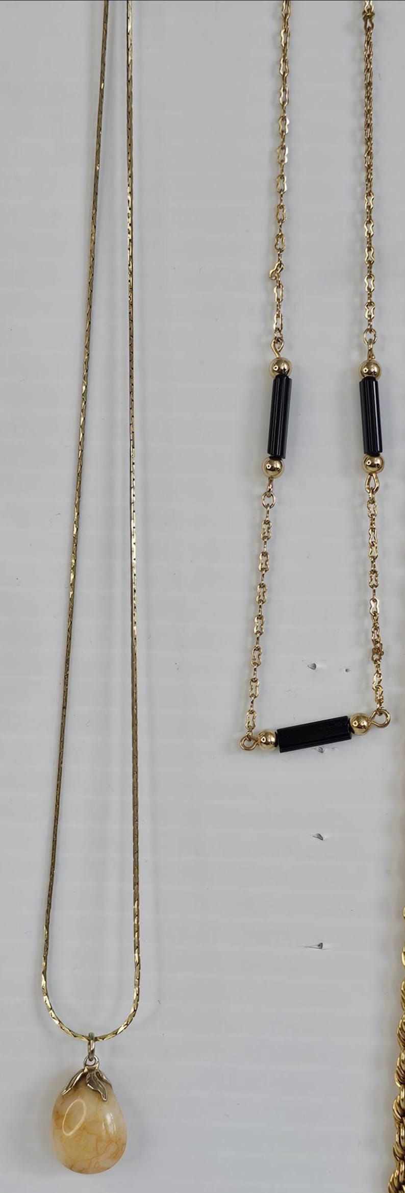 May include: A collection of gold-toned necklaces. One features a teardrop-shaped pendant, while others have delicate chains. One necklace has black rectangular beads.