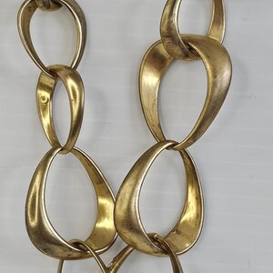 May include: Gold-toned statement necklace featuring large, interconnected oval links. One link is embellished with sparkling rhinestones. The necklace has a vintage aesthetic and is suitable for special occasions or adding a touch of glamour to any outfit.