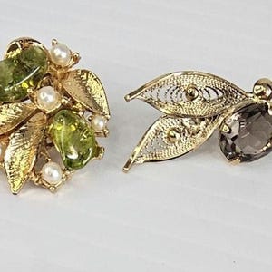 May include: Four pairs of vintage earrings. Two pairs feature gold-toned metal with green and clear stones, and faux pearls. The other two pairs have gold filigree leaves with dark gray stones.