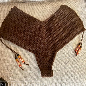 May include: A brown crochet bottom with a V-shaped front and beaded ties. The handmade garment is displayed on a neutral-colored surface. The text "SUNDAYCOZYCROCHET" is visible in the bottom left corner.