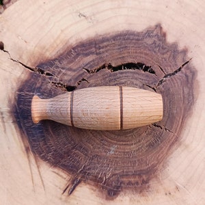 Könnte beinhalten: Ein hölzerner Vogellauf mit brauner Oberfläche und zwei dunkelbraunen Bändern um die Mitte. Der Ruf liegt auf einer Holzoberfläche mit natürlicher Holzmaserung.