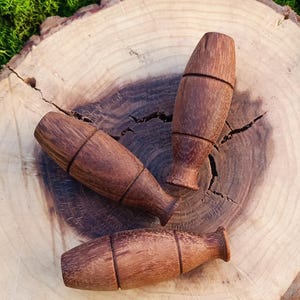 Könnte beinhalten: Drei Flaschenverschlüsse aus Holz in verschiedenen Formen und Größen, mit einer natürlichen Holzoptik, sind auf einer Holzscheibe angeordnet. Die Verschlüsse haben alle unterschiedliche Formen, aber sie sind alle aus der gleichen Holzart gefertigt.