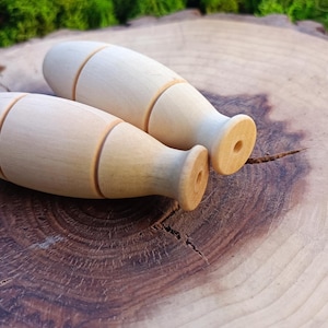 Puede incluir: Dos remates decorativos de madera, de color marrón claro, con una banda marrón claro alrededor del centro. Los remates están sobre una superficie de madera.