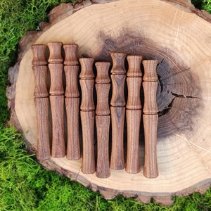 Peut inclure: Ensemble de neuf bouchons de bouteille en bois tourné, chacun avec un design décoratif unique. Les bouchons sont disposés sur une tranche de bois naturelle, sur un fond de mousse verte vibrante. Le bois est brun chaud.