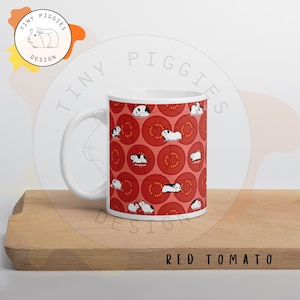 May include: White ceramic mug with a repeating pattern of red tomato slices and guinea pigs. The mug has a white handle and the text "RED TOMATO" is at the bottom. The mug is a Tiny Piggie Design.